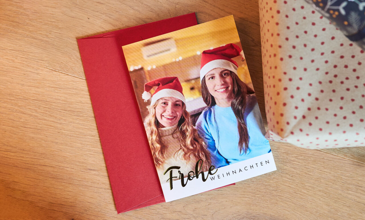 Zwei Personen mit Weihnachtsmützen präsentieren eine frohe Weihnachtskarte.